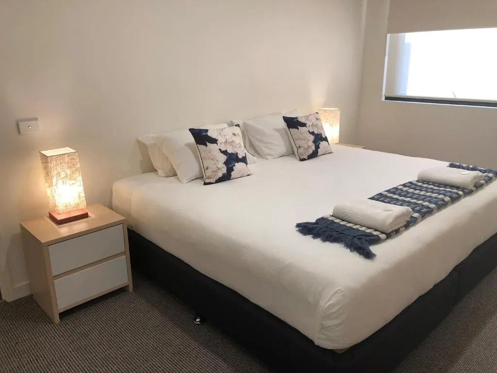 King bed in apartment bedroom with navy floral cushions and bedside lamp